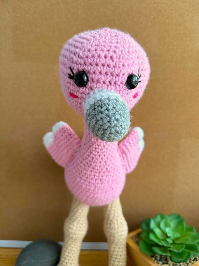 handmade crochet tall pink flamingo with rosy cheeks, long legs, and fluffy wings