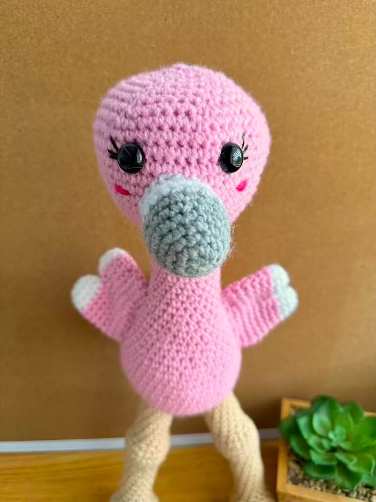 handmade crochet tall pink flamingo with rosy cheeks, long legs, and fluffy wings