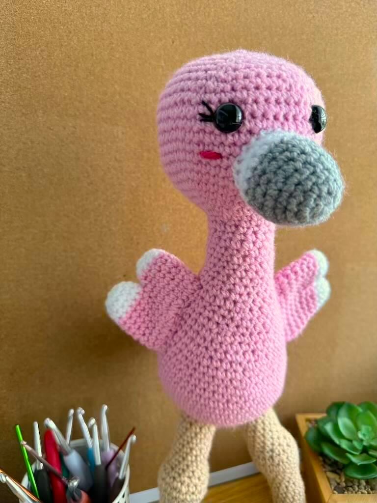 handmade crochet tall pink flamingo with rosy cheeks, long legs, and fluffy wings